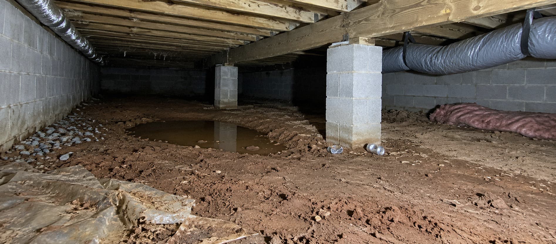 A rendering of an untreated crawlspace floor before the work: wet red clay, loose stones, a sagging insulation batt and torn old plastic along the walls